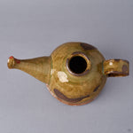 Top view of a Kyoto ware earthenware sake carafe, short upright mouth, ochre Oribe-green crackle glaze, looped handle and spout, gold-and-silver plum blossom at the spout.