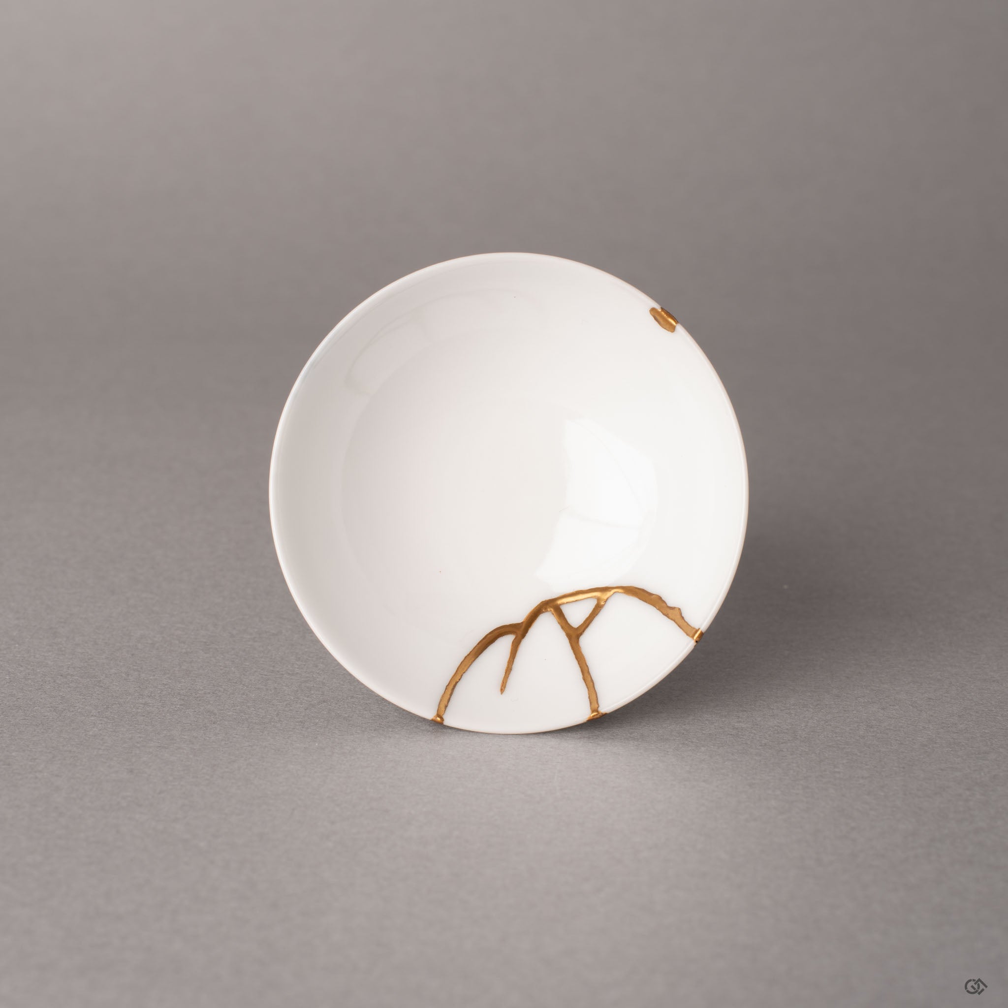 Top view of a kintsugi Arita sake cup revealing branching gold seams radiating across the white interior, heritage luxury from Japan.