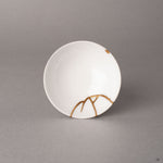 Top view of a kintsugi Arita sake cup revealing branching gold seams radiating across the white interior, heritage luxury from Japan.