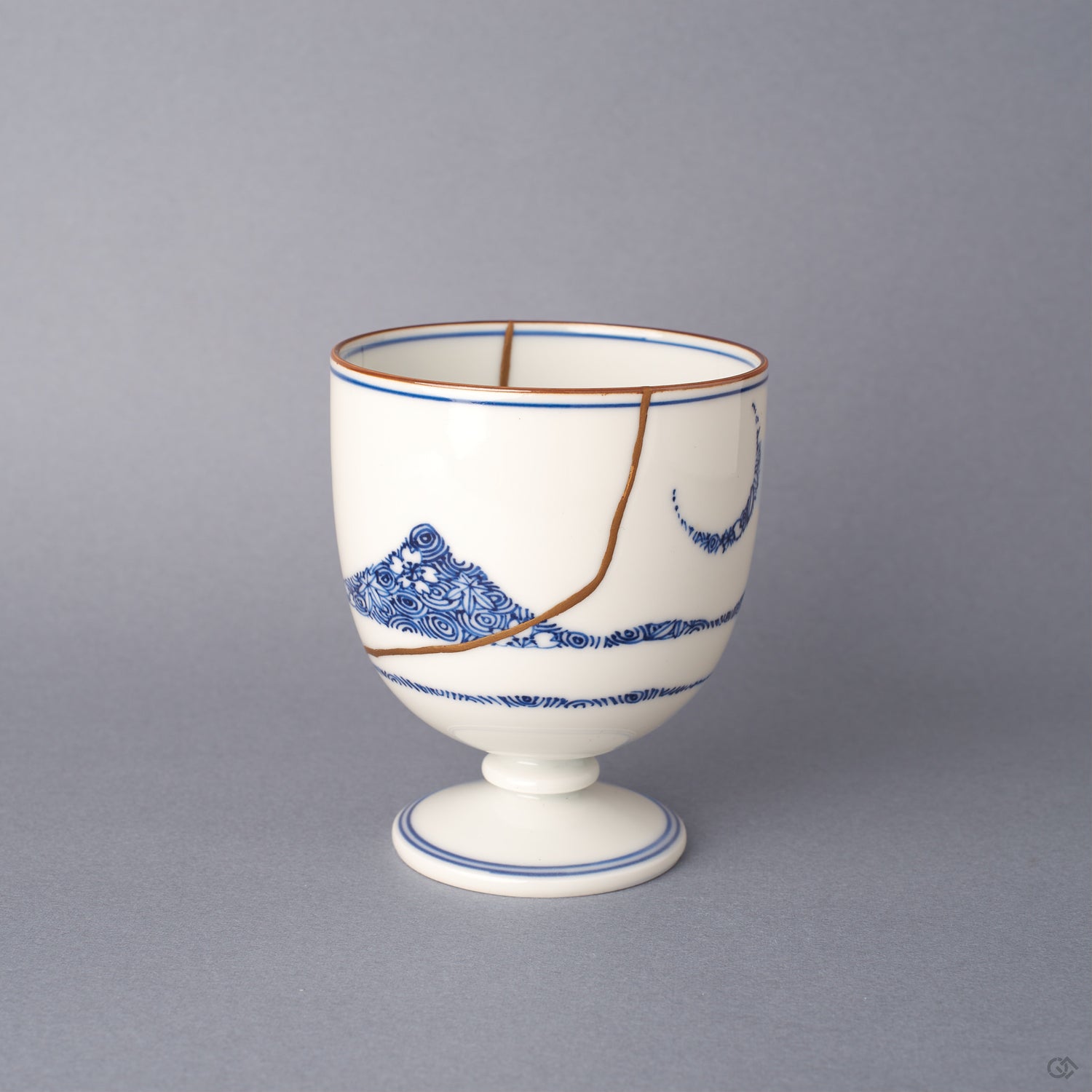 Front view of an Arita ware sake cup in white porcelain, cobalt-blue sometsuke bands and a floral roundel, with 24K gold kintsugi seams crossing the rounded body.
