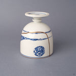 Side view of a footed Arita ware sake cup in white porcelain, its 24K gold kintsugi seams crossing cobalt-blue patterned bands around the body.