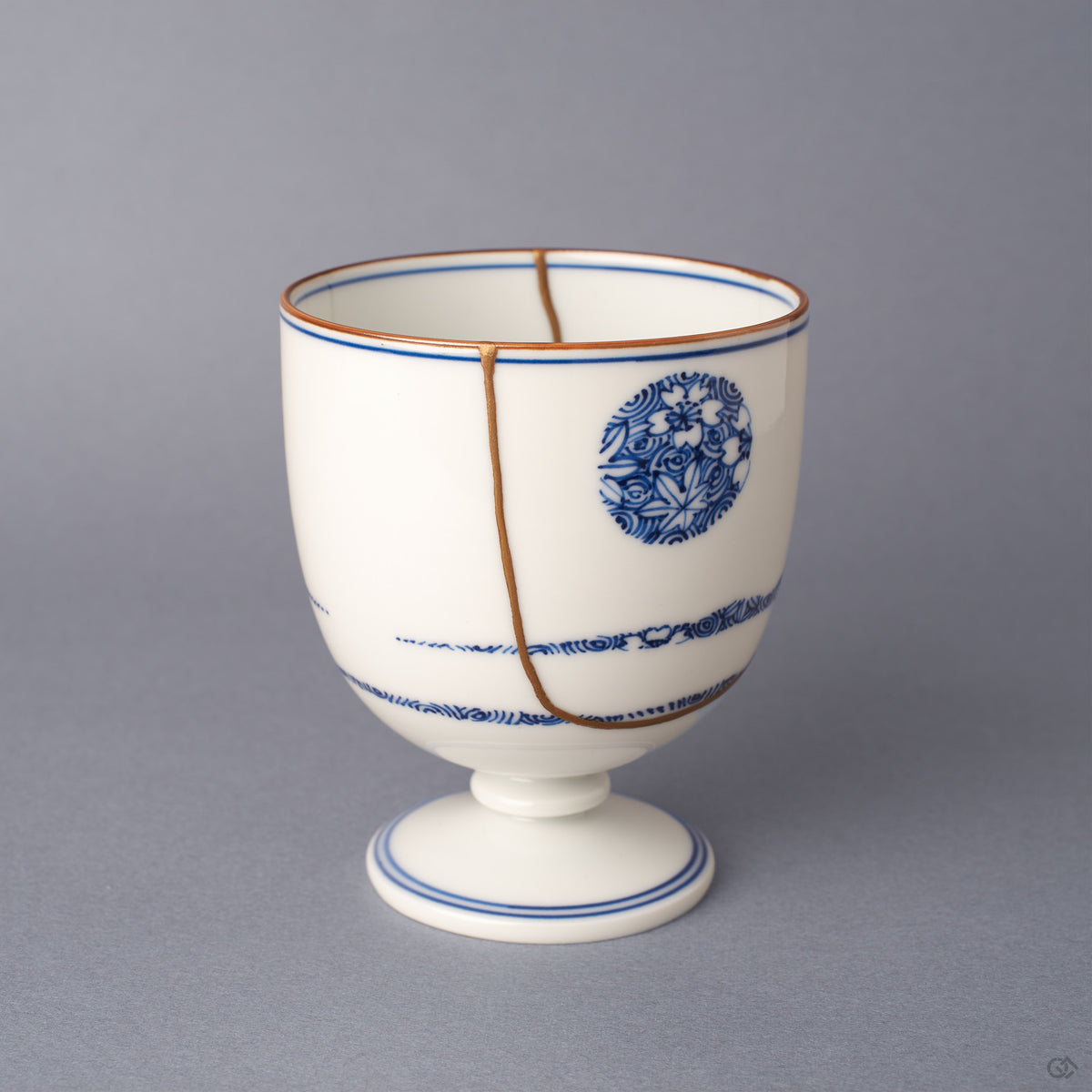 Alternate side view of the Arita ware sake cup, a vertical 24K gold kintsugi seam descending from rim to foot beside a cobalt-blue floral roundel on white porcelain.