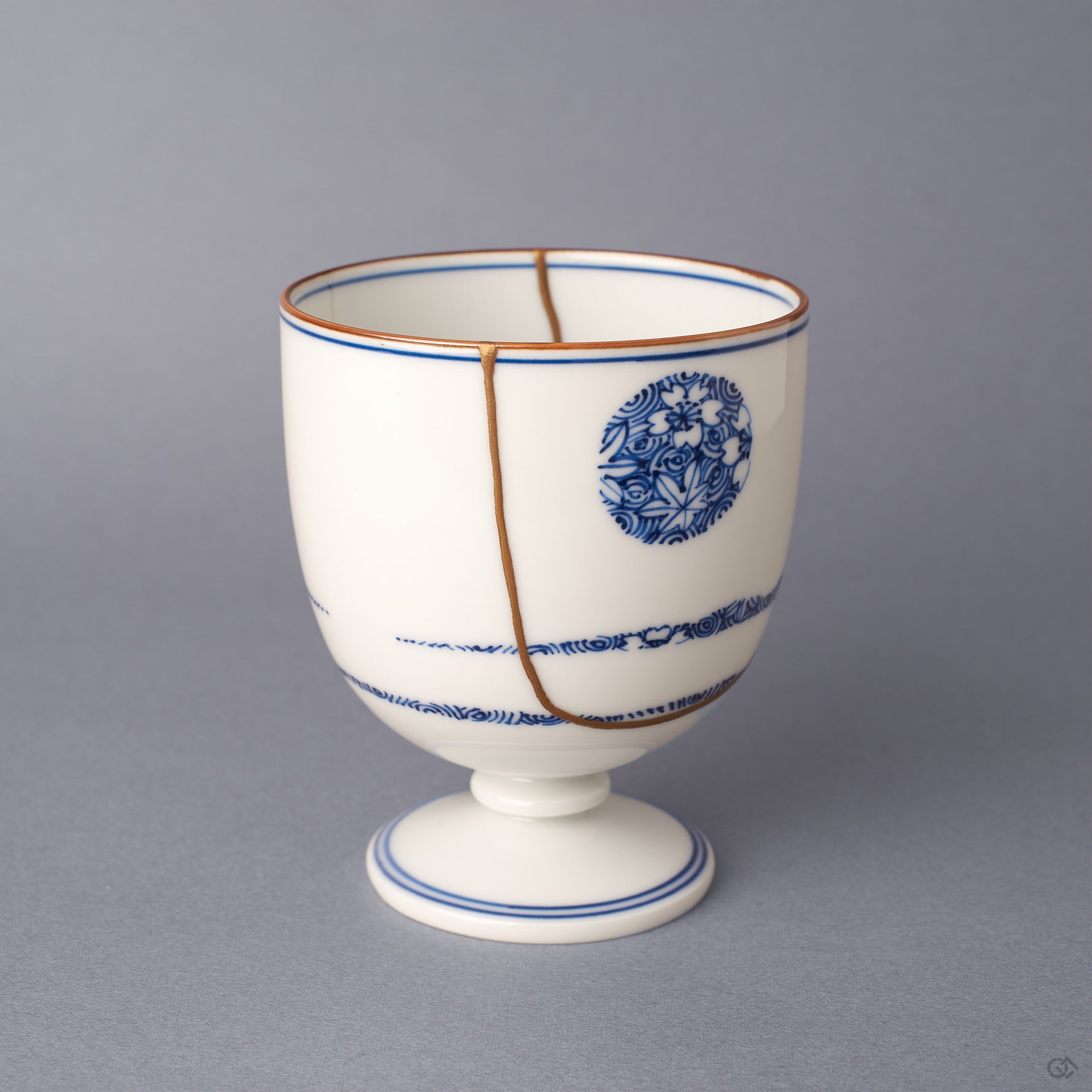 Alternate side view of the Arita ware sake cup, a vertical 24K gold kintsugi seam descending from rim to foot beside a cobalt-blue floral roundel on white porcelain.