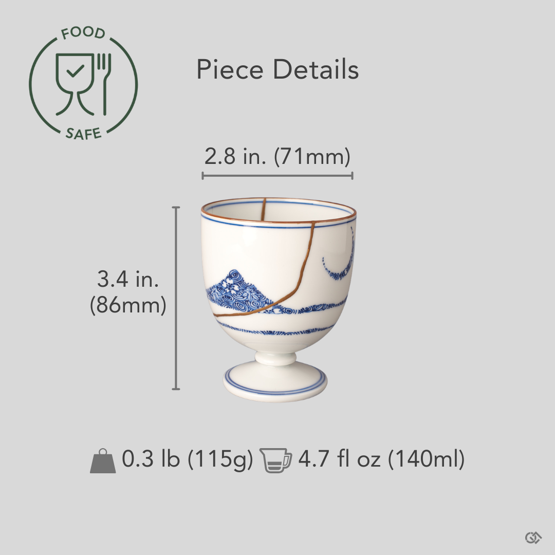 Arita ware sake cup in white porcelain with cobalt-blue bands and 24K gold kintsugi seams, restored with natural urushi, shown beside an object for scale reference.