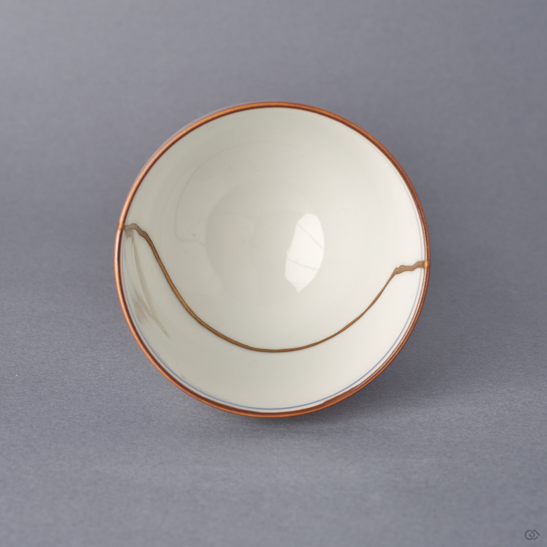 Top-down view into the Arita ware sake cup, a sweeping 24K gold kintsugi seam arcing across the white porcelain interior within an iron-brown rim line.