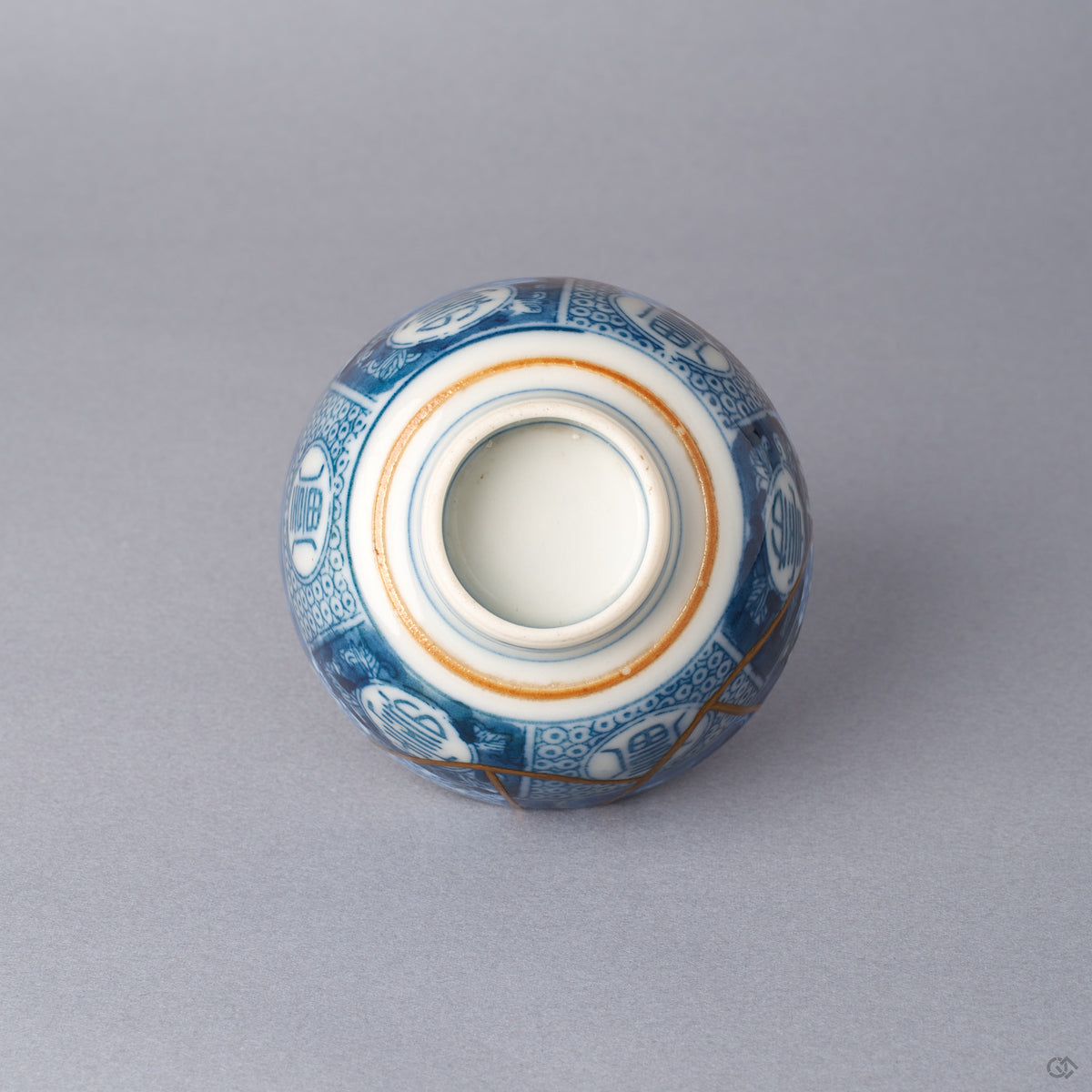 Bottom view of a Ko-Imari sake cup showing the unglazed foot ring, gold-lined bands around the base, blue sometsuke medallions, and a 24K gold kintsugi seam crossing the body.