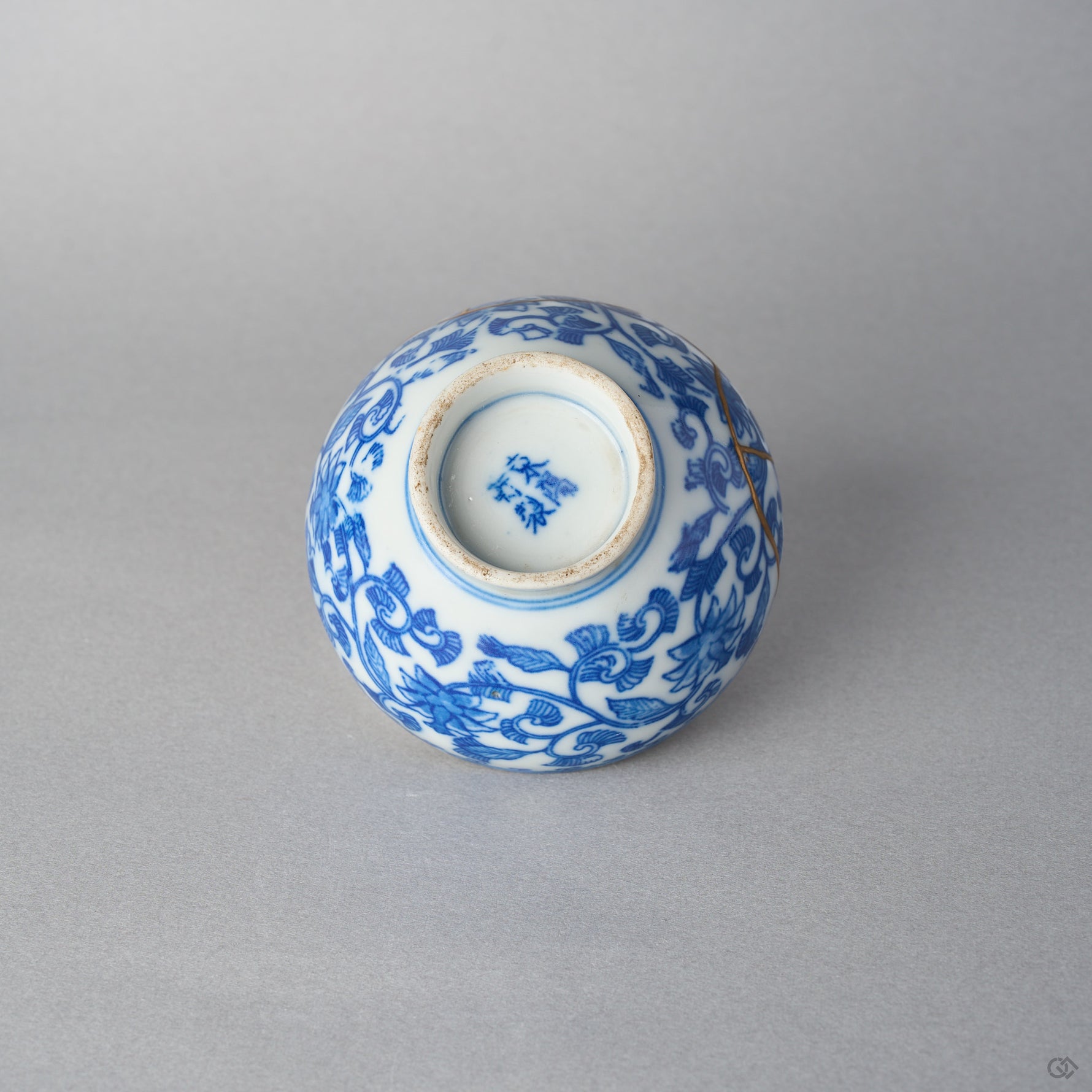 Underside of an Edo-period Ko-Imari sake cup with a cobalt mark inside the worn footring, karakusa vines and a gold kintsugi seam on the body.