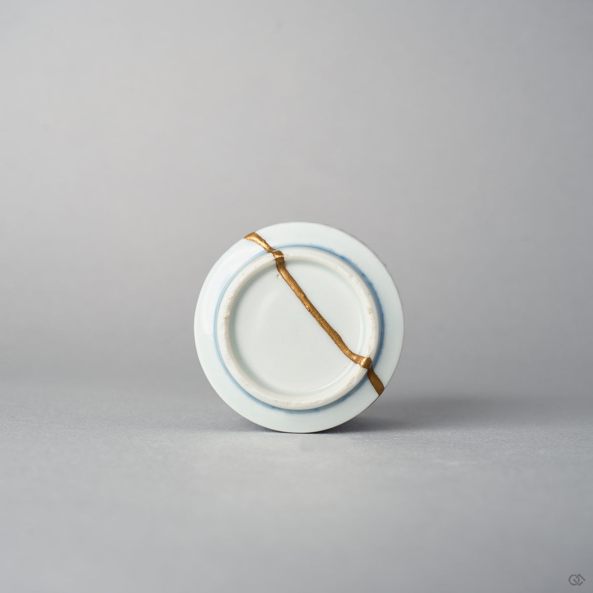 Bottom view of a Ko-Imari sake cup showing a 24K gold kintsugi line crossing the unglazed foot ring and base of the blue takokarakusa porcelain, restored with natural urushi.