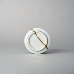 Bottom view of a Ko-Imari sake cup showing a 24K gold kintsugi line crossing the unglazed foot ring and base of the blue takokarakusa porcelain, restored with natural urushi.
