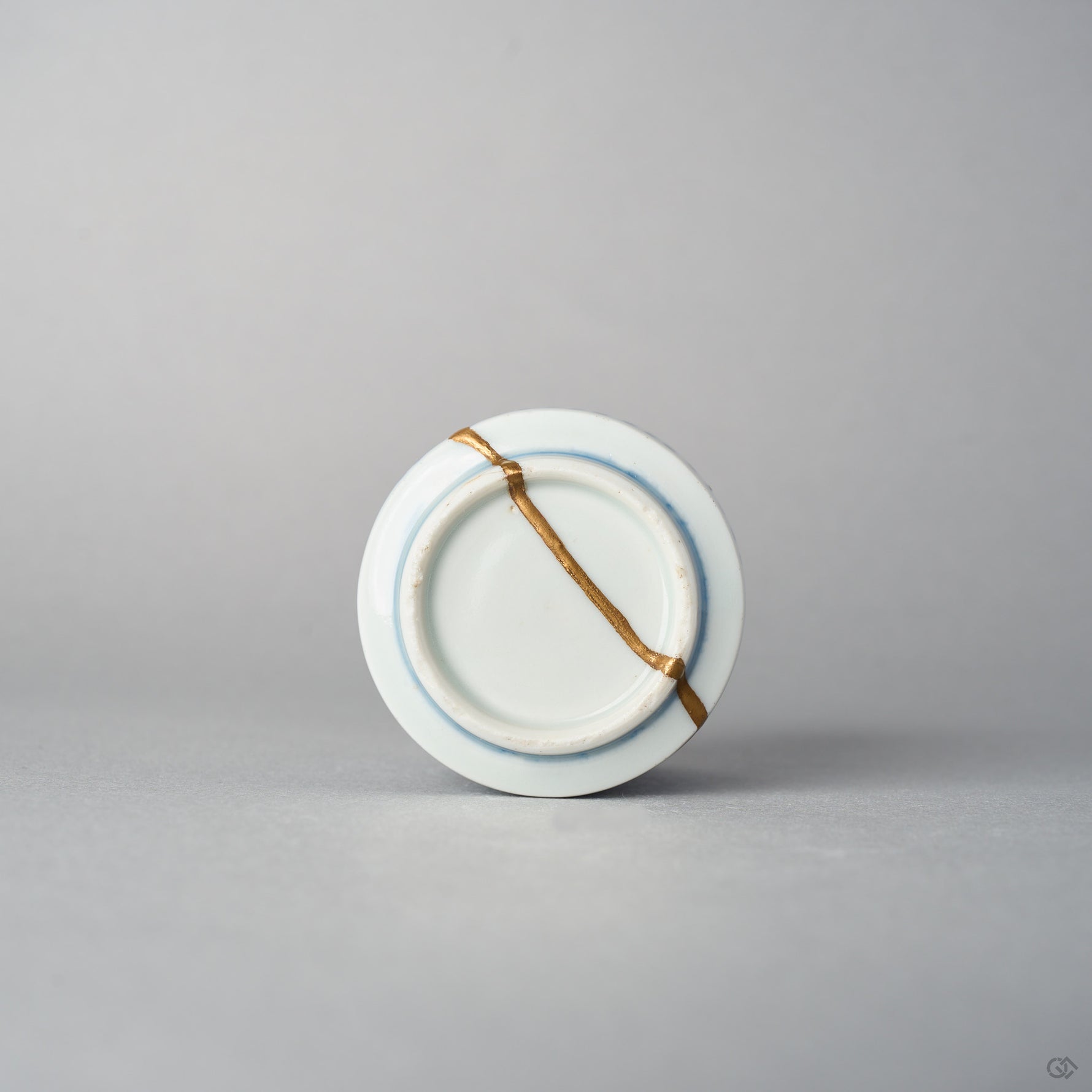 Bottom view of a Ko-Imari sake cup showing a 24K gold kintsugi line crossing the unglazed foot ring and base of the blue takokarakusa porcelain, restored with natural urushi.