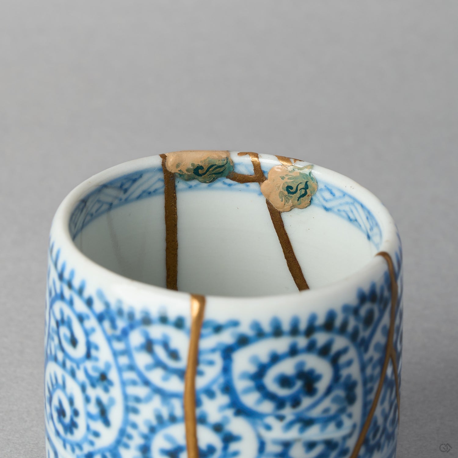 Close-up of the rim of a Ko-Imari sake cup: cloud motifs in takamaki-e relief with kawari-nuri texture and blue urushi beside 24K gold kintsugi lines on blue takokarakusa porcelain.