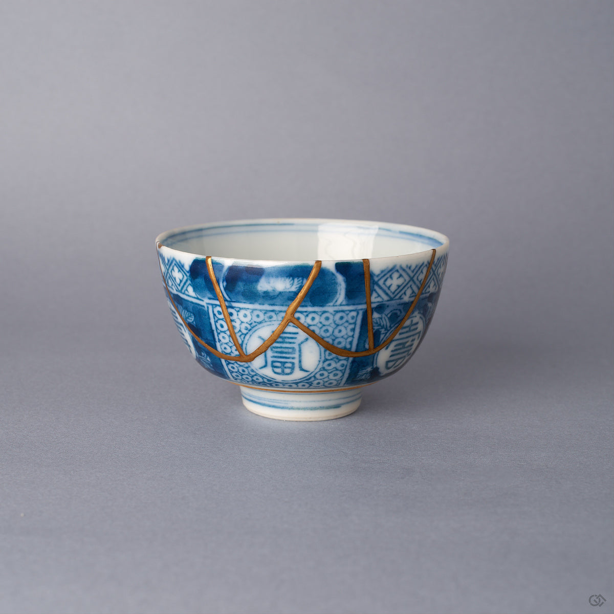 Front view of a blue and white Ko-Imari sake cup with 24K gold kintsugi seams arcing down from the rim across cobalt panels and longevity medallions, restored with natural urushi.