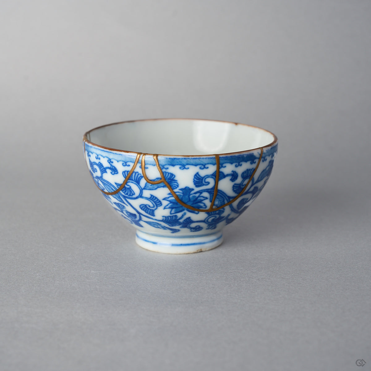 Front view of an Edo-period Ko-Imari sake cup, hand-painted karakusa vines in cobalt under a wave border, 24K gold kintsugi arcs draped from the rim.