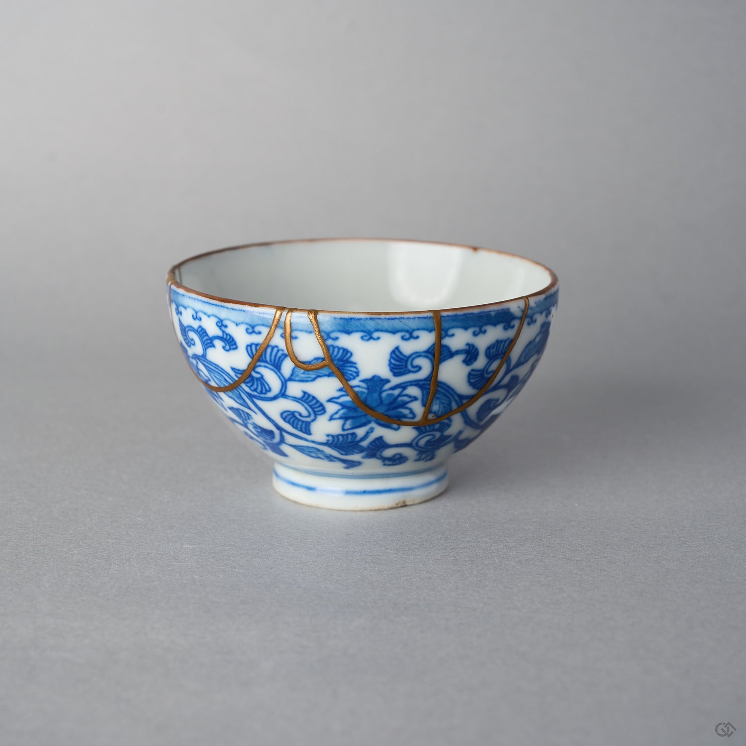 Front view of an Edo-period Ko-Imari sake cup, hand-painted karakusa vines in cobalt under a wave border, 24K gold kintsugi arcs draped from the rim.