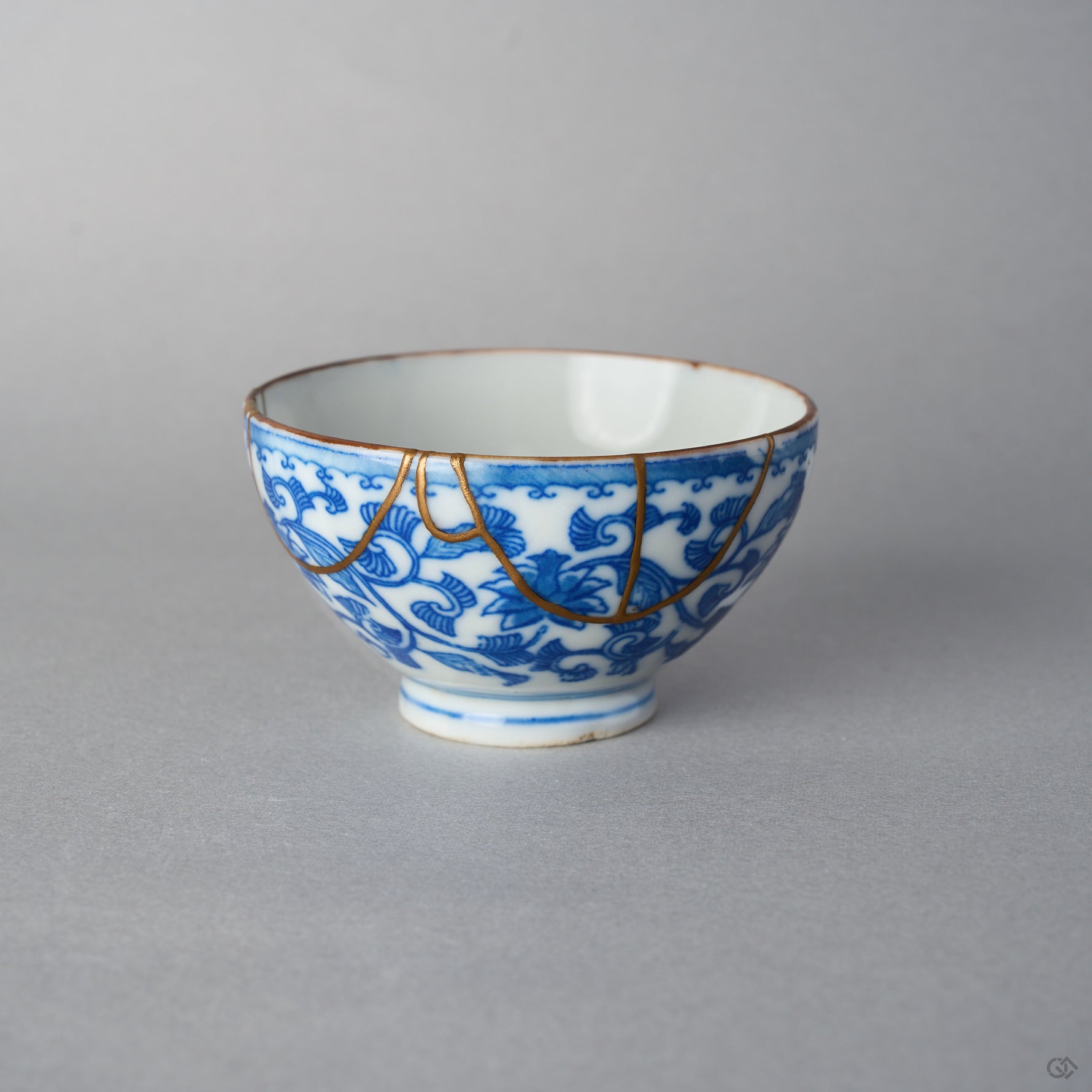 Front view of an Edo-period Ko-Imari sake cup, hand-painted karakusa vines in cobalt under a wave border, 24K gold kintsugi arcs draped from the rim.