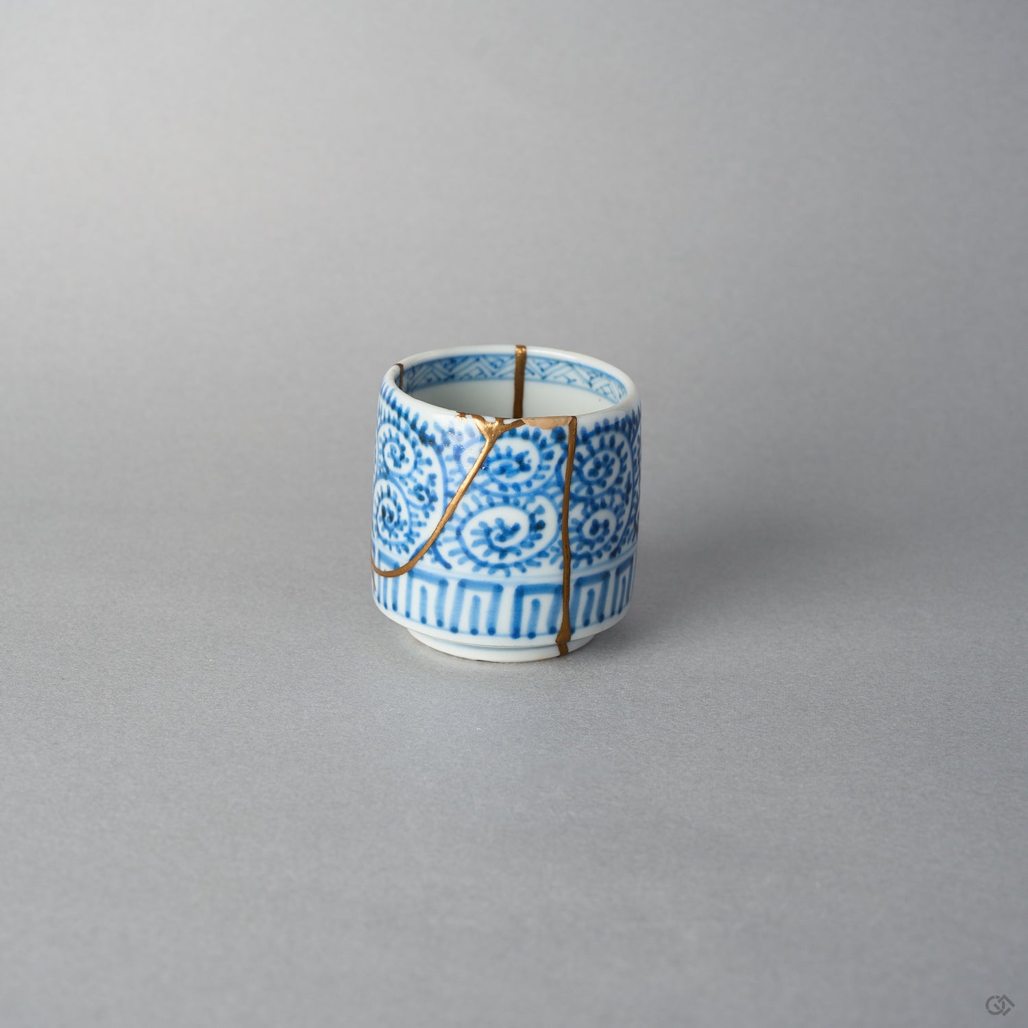 Front view of a Ko-Imari sake cup in sometsuke blue takokarakusa porcelain, 24K gold kintsugi lines rising from foot to rim through the scrolling vines, restored with natural urushi.
