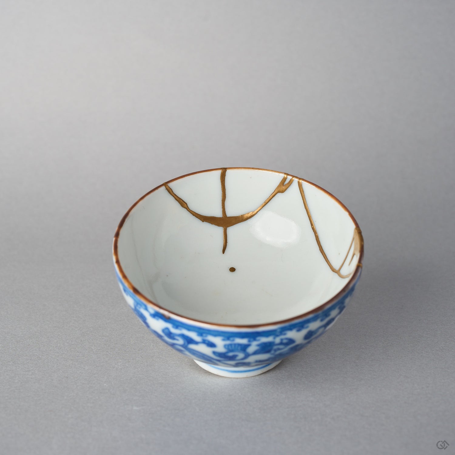 Interior of a Ko-Imari sake cup, branching 24K gold kintsugi lines crossing the plain white well toward a single gold drop near the center.