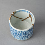 Interior close-up of a Ko-Imari sake cup showing 24K gold kintsugi lines descending the white porcelain wall from a rim ringed in blue, restored with 100% natural urushi.