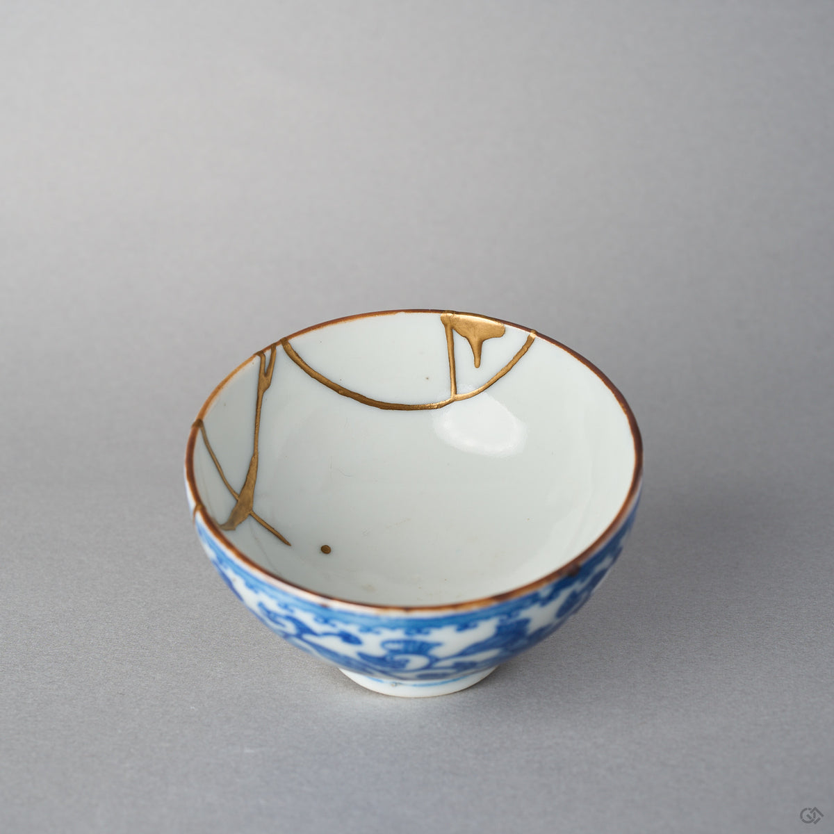Close view inside an Edo-period Ko-Imari sake cup, gold kintsugi seams meeting the brown-edged rim and settling as a small drop in the white glaze.