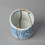 Interior close-up of a Ko-Imari sake cup with branching 24K gold kintsugi lines crossing the white well beneath a sometsuke blue border, restored with natural urushi in Japan.