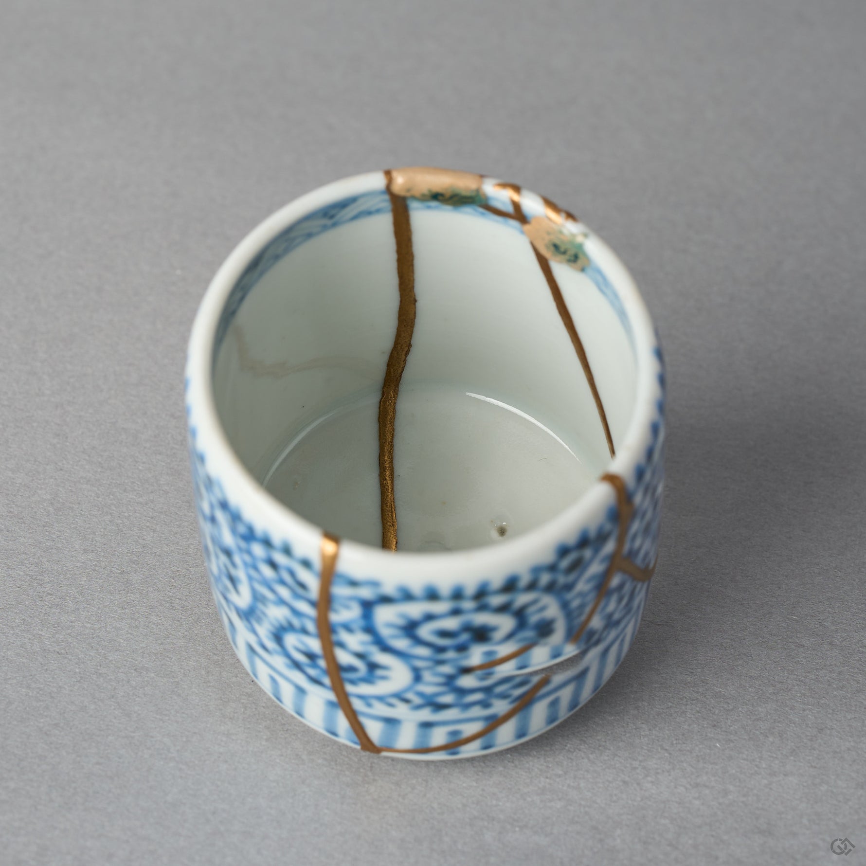 Interior close-up of a Ko-Imari sake cup with branching 24K gold kintsugi lines crossing the white well beneath a sometsuke blue border, restored with natural urushi in Japan.