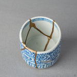 Interior view of a Ko-Imari sake cup where 24K gold kintsugi lines meet across the white porcelain floor, blue takokarakusa scrolls circling the outer wall, restored with urushi.