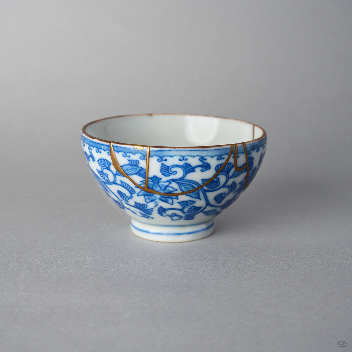 Side view of a kintsugi Ko-Imari sake cup showing shaded sometsuke vines and a 24K gold restoration line arcing across the painted exterior.
