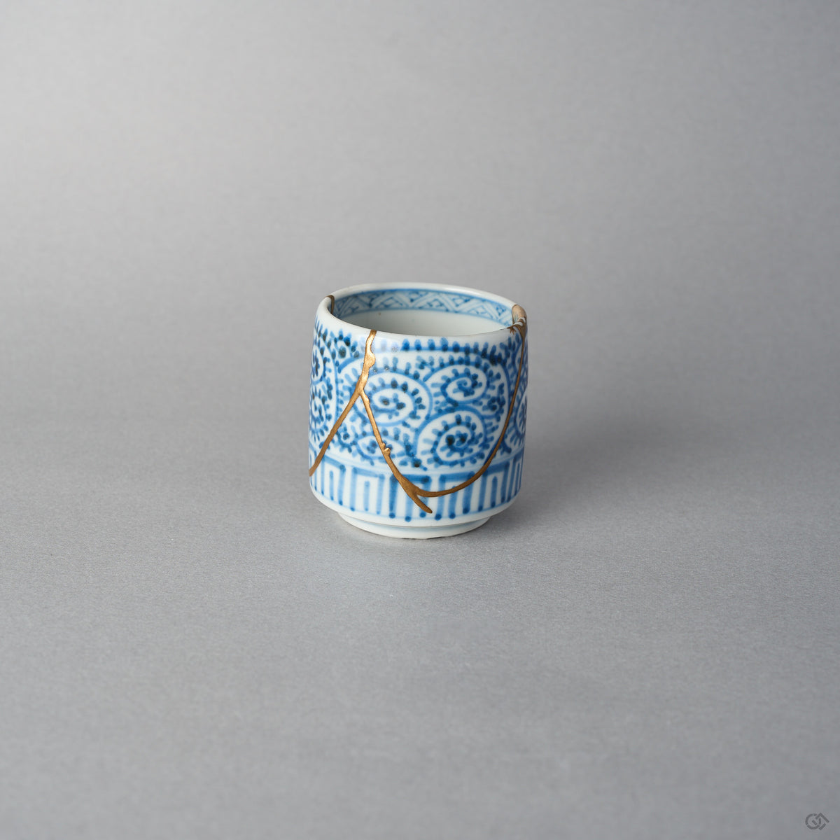 Side view of a Ko-Imari sake cup covered in blue takokarakusa scrolls, a branching 24K gold kintsugi line arcing across the pattern, restored with 100% natural urushi in Japan.