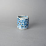 Side view of a Ko-Imari sake cup covered in blue takokarakusa scrolls, a branching 24K gold kintsugi line arcing across the pattern, restored with 100% natural urushi in Japan.