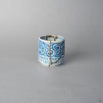 Side view of a Ko-Imari sake cup in blue takokarakusa porcelain showing raised lacquer cloud motifs at the rim above 24K gold kintsugi seams, restored with natural urushi.