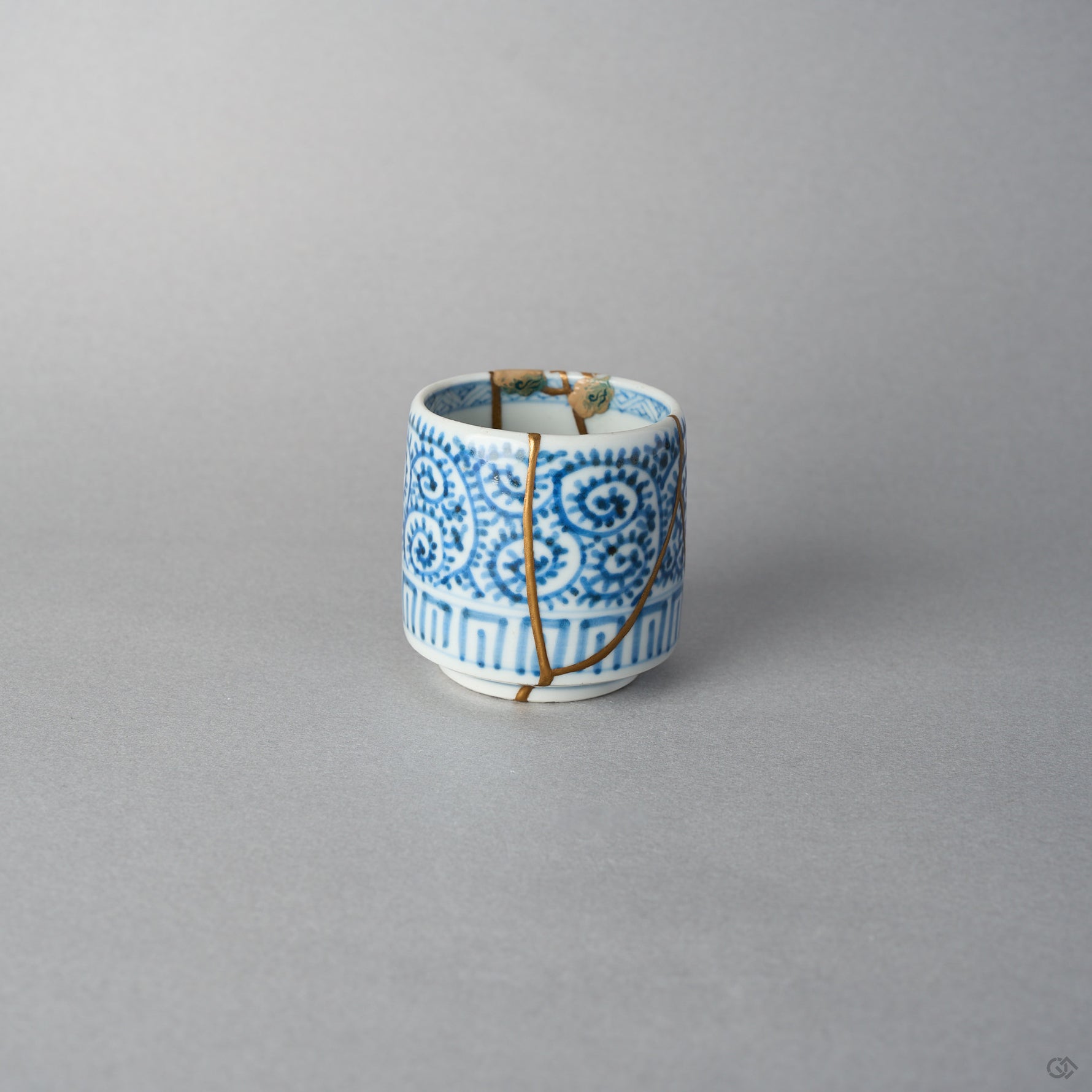 Side view of a Ko-Imari sake cup in blue takokarakusa porcelain showing raised lacquer cloud motifs at the rim above 24K gold kintsugi seams, restored with natural urushi.