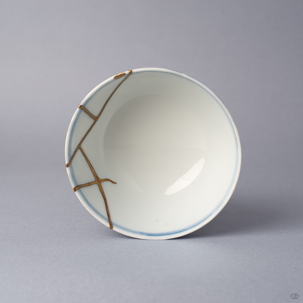 Top view into a Ko-Imari sake cup, the white interior crossed near the rim by angular 24K gold kintsugi lines that join where the broken pieces were reassembled with urushi.