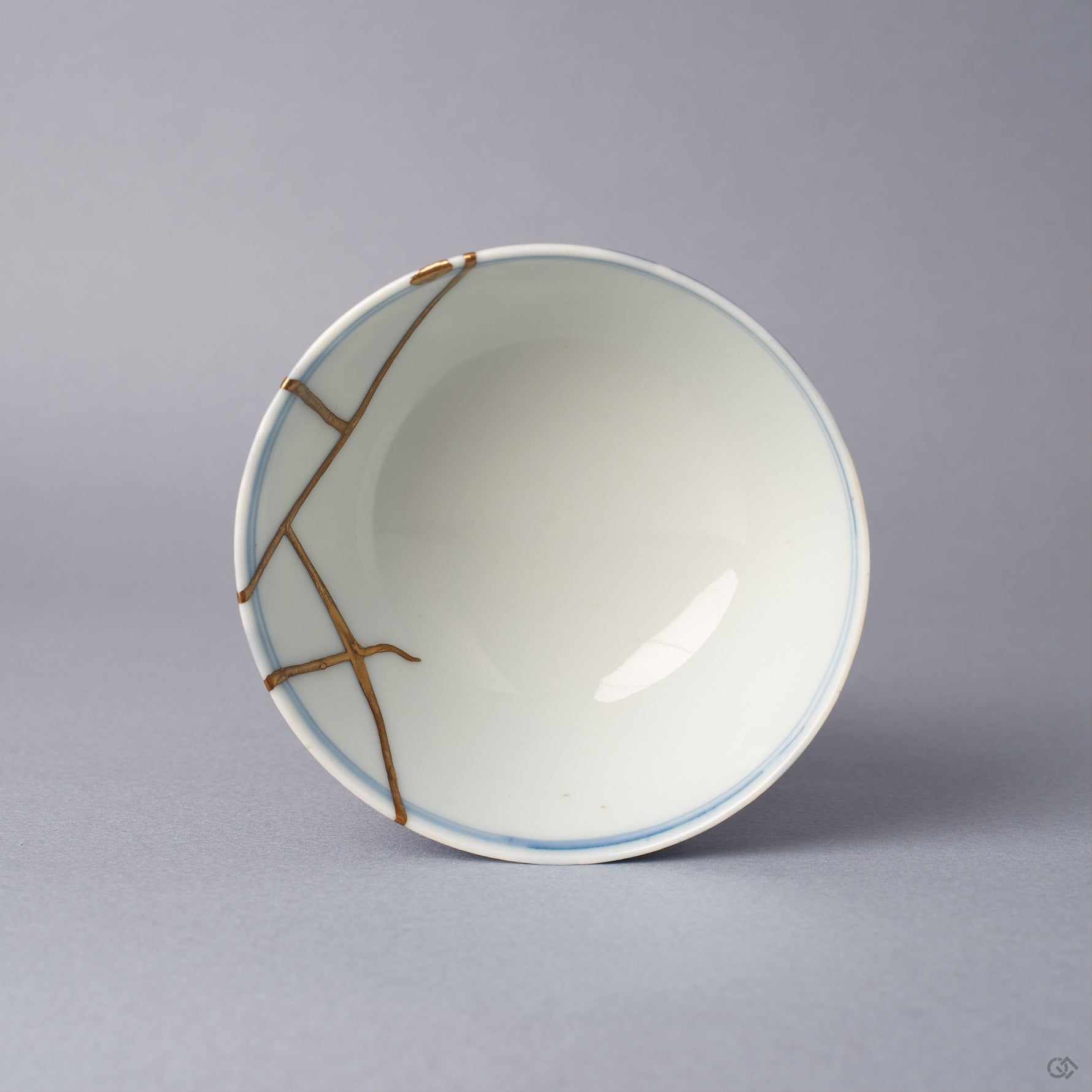 Top view into a Ko-Imari sake cup, the white interior crossed near the rim by angular 24K gold kintsugi lines that join where the broken pieces were reassembled with urushi.