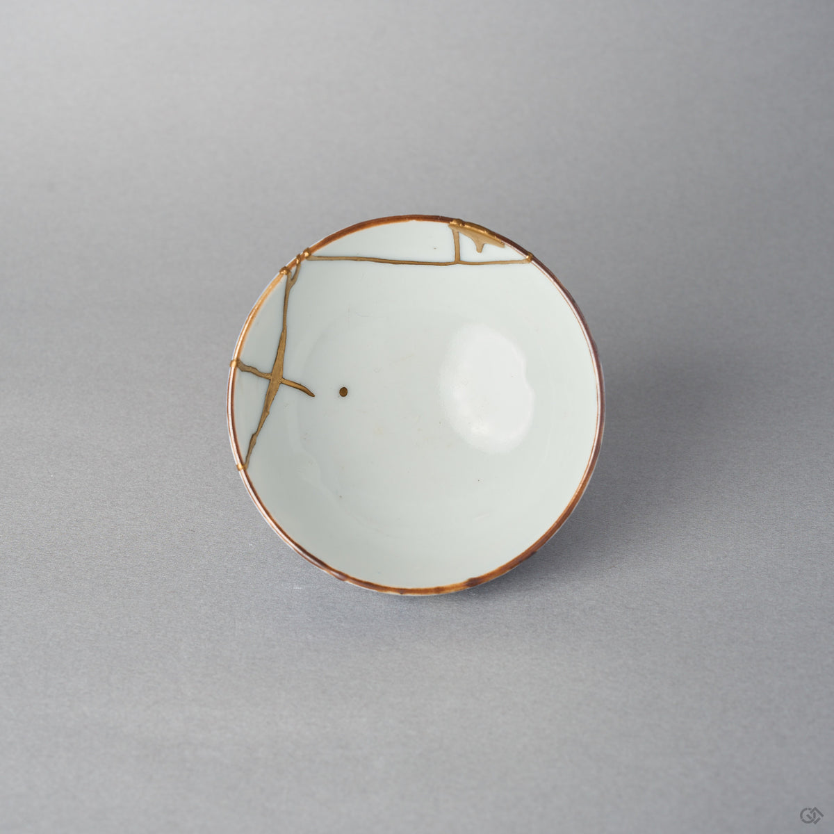 Top view of a kintsugi Ko-Imari sake cup, the white interior crossed by 24K gold restoration lines with a single gold drop resting near the well.