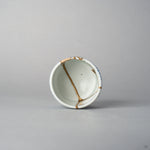 Top view of a Ko-Imari sake cup showing 24K gold kintsugi lines converging inside the white well, the rim and outer wall patterned in sometsuke blue takokarakusa, urushi-restored.