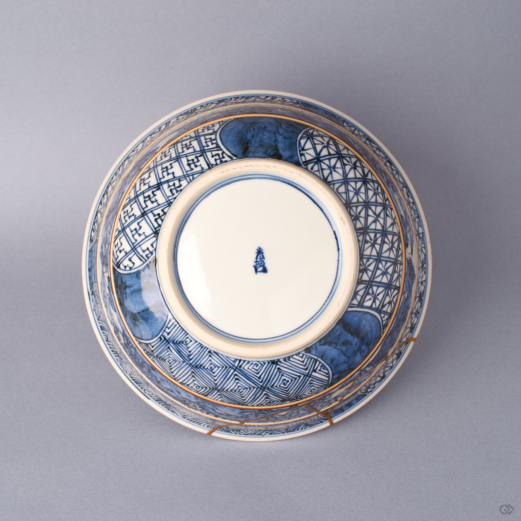 Underside of the sometsuke porcelain serving bowl with banded patterns, a blue kiln mark on the foot, and 24K gold kintsugi lines crossing the lower body.