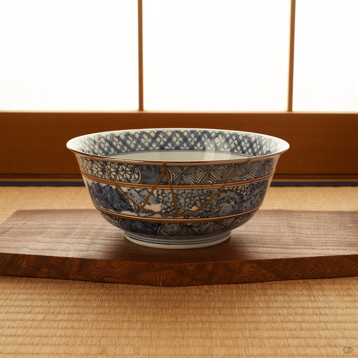 Kyoto ware kintsugi serving bowl in sometsuke blue resting on a wooden stand on tatami before a shoji screen, its 24K gold seam visible on the banded body.