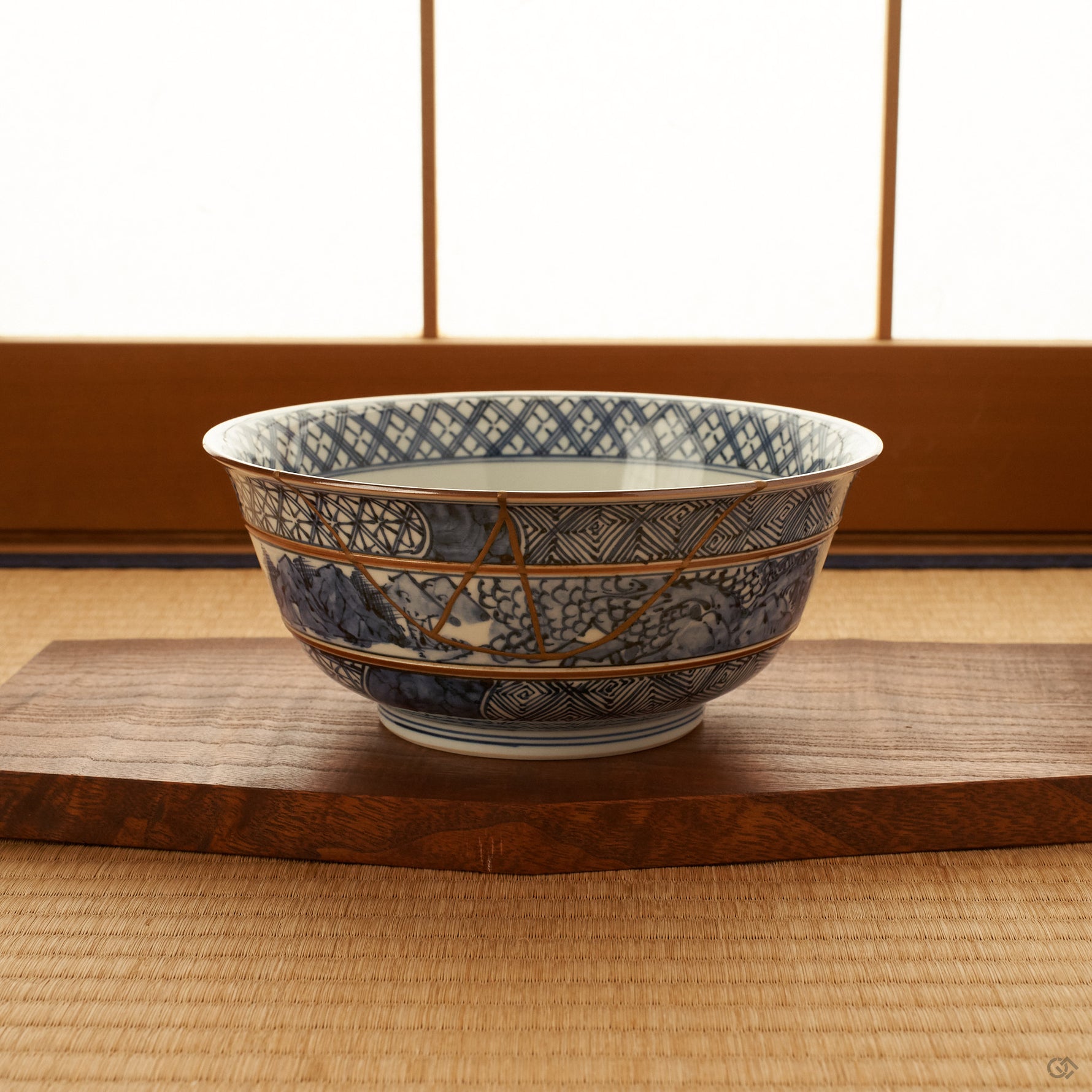 Kyoto ware kintsugi serving bowl in sometsuke blue resting on a wooden stand on tatami before a shoji screen, its 24K gold seam visible on the banded body.