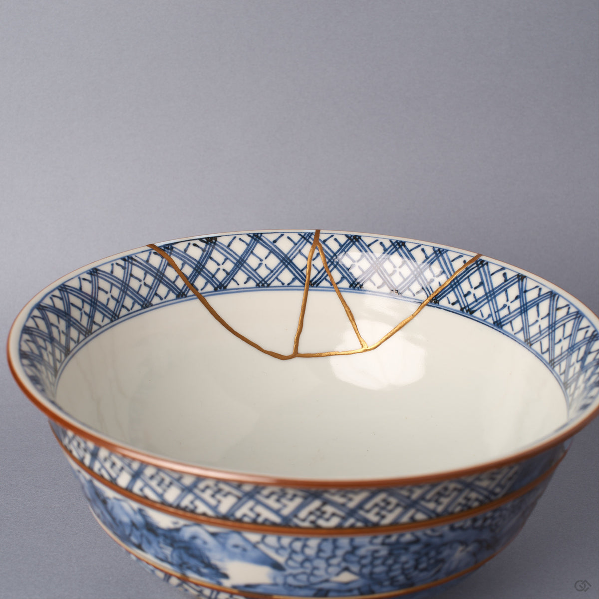 Interior of the sometsuke serving bowl, its white glaze framed by a blue lattice rim band, with the branching 24K gold kintsugi seam descending toward the well.