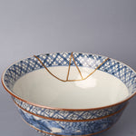 Interior of the sometsuke serving bowl, its white glaze framed by a blue lattice rim band, with the branching 24K gold kintsugi seam descending toward the well.
