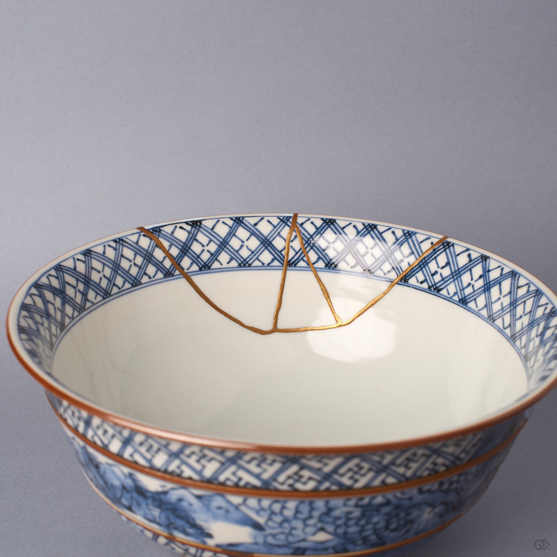 Interior of the sometsuke serving bowl, its white glaze framed by a blue lattice rim band, with the branching 24K gold kintsugi seam descending toward the well.