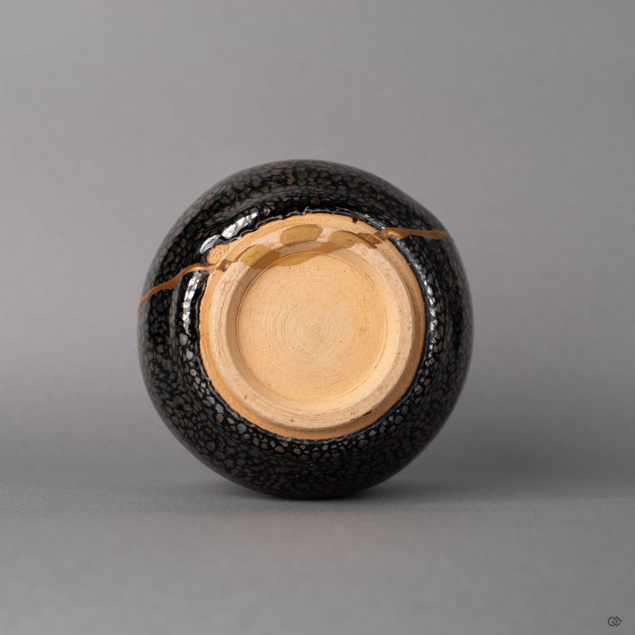 The foot ring of this Kyoto tenmoku cup grounds the vessel, kiln-fired texture meeting kintsugi gold, history made visible below.