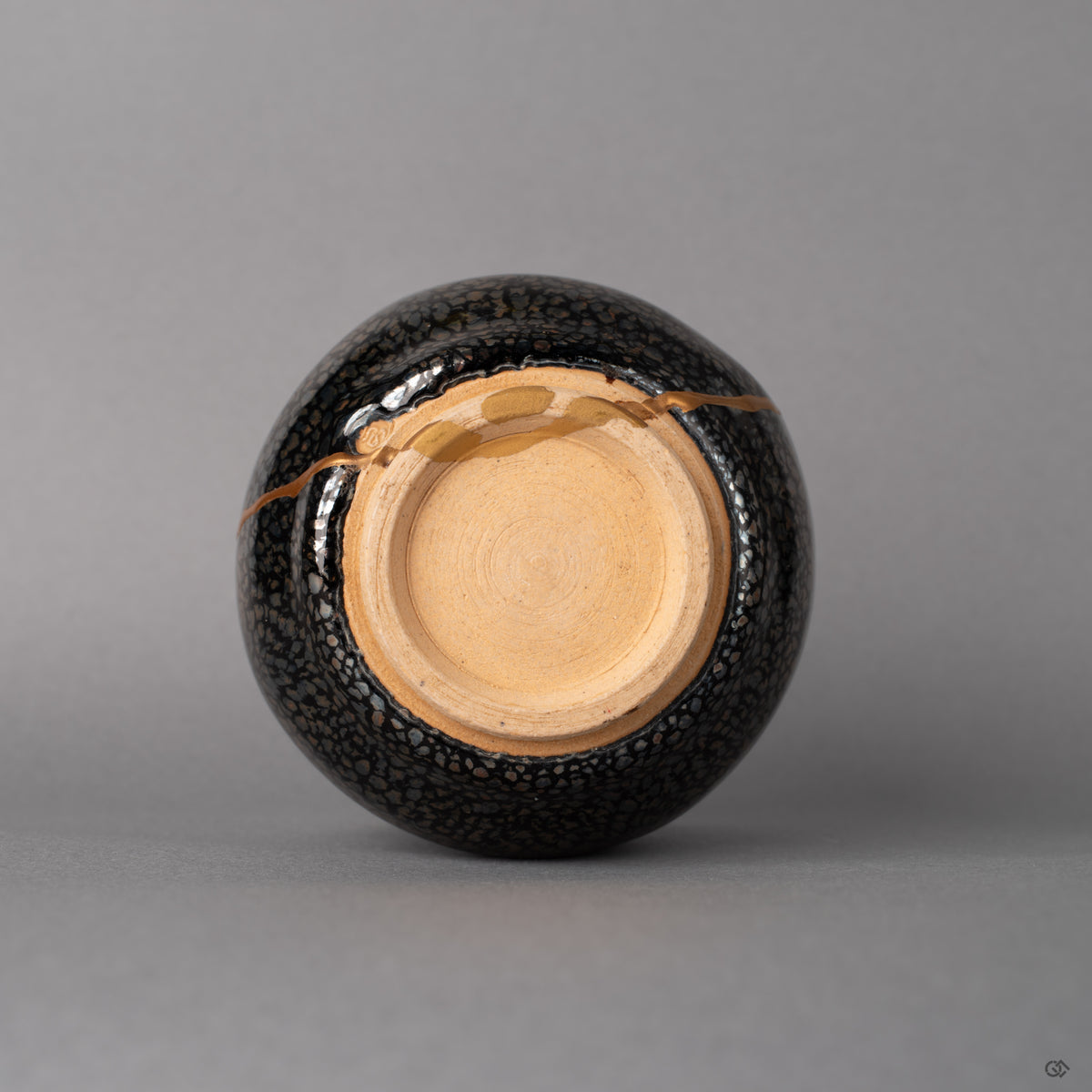 The foot ring of this Kyoto tenmoku cup grounds the vessel, kiln-fired texture meeting kintsugi gold, history made visible below.