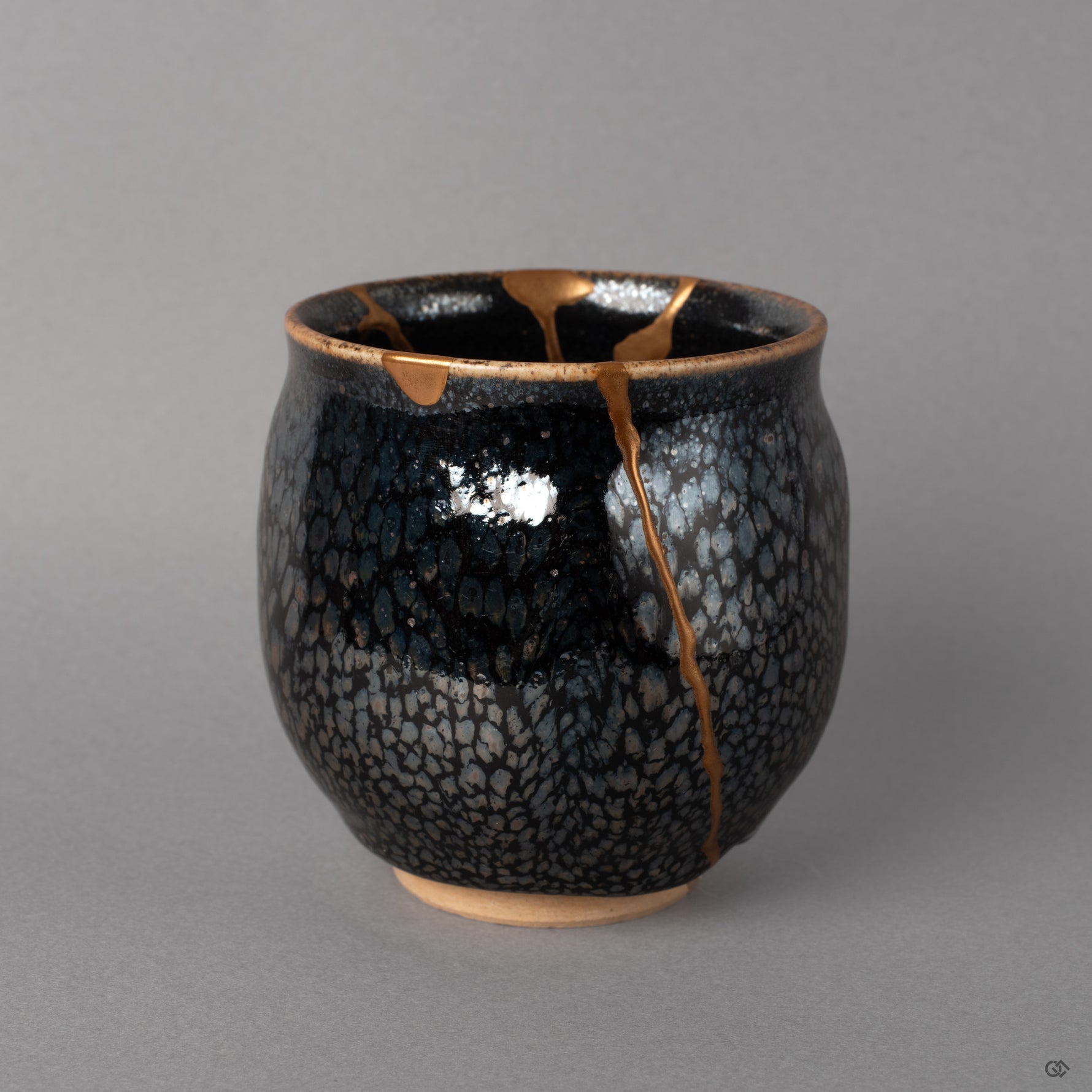 Silver flecks scatter across the tenmoku surface like distant stars, kintsugi gold crossing between, beauty in imperfection up close.