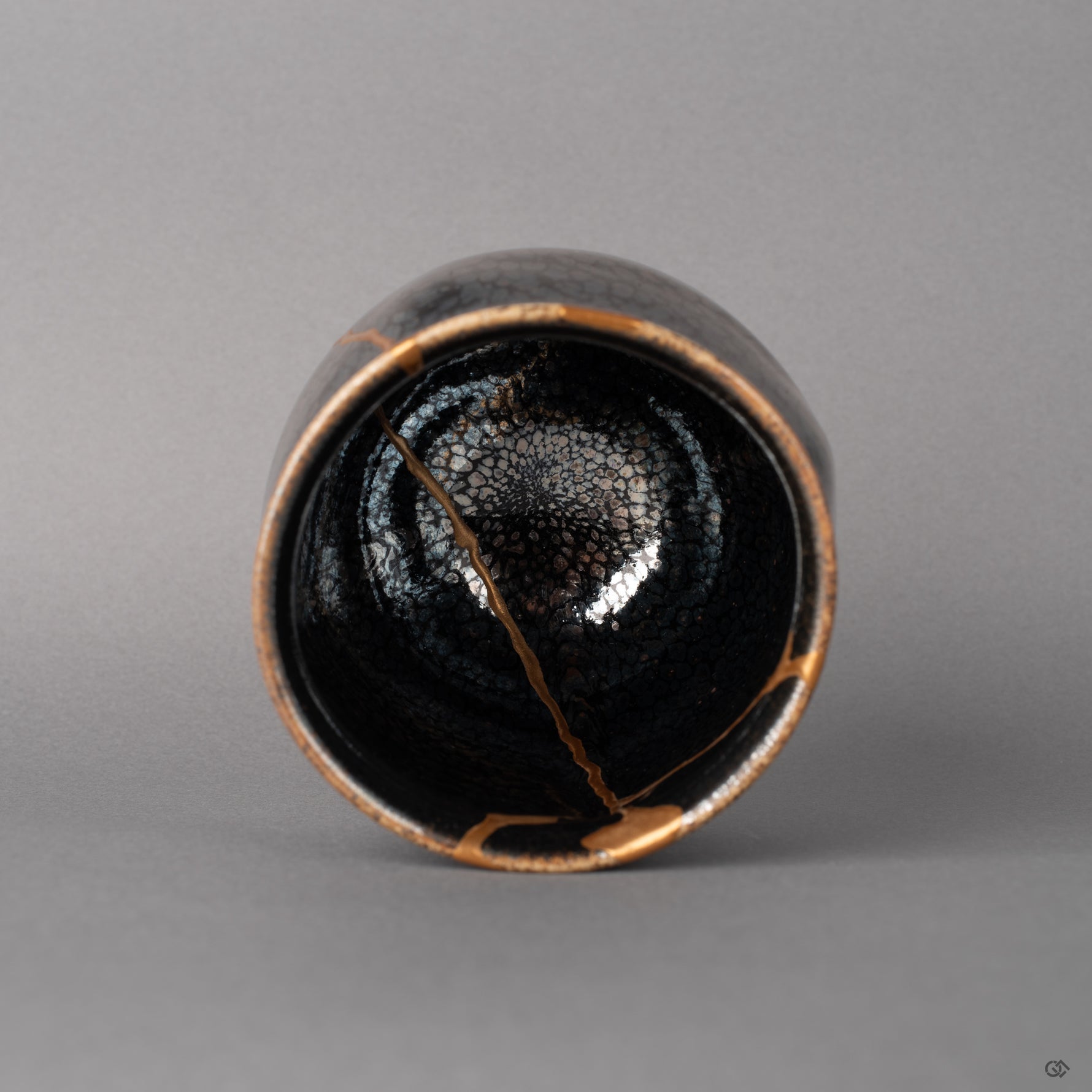 From above, the tenmoku cup reveals scattered silver flecks and kintsugi lines descending inward, a quiet beauty in the round.