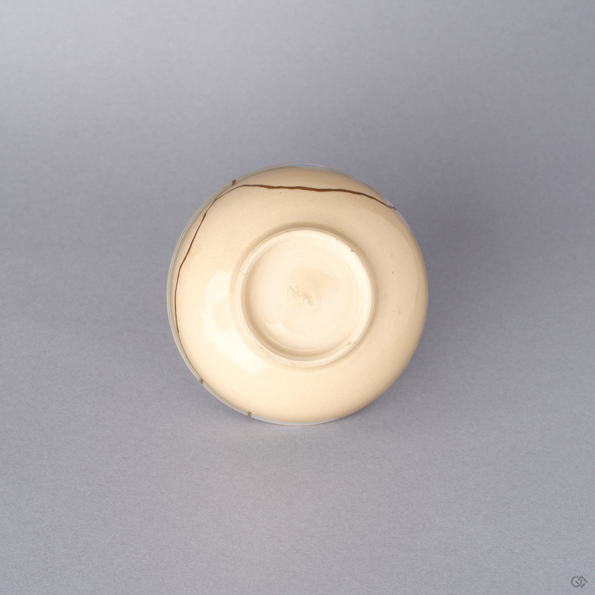 Bottom view of the cream colored Kyoto ware kintsugi cup, showing the small trimmed foot ring of the earthenware vessel restored with natural urushi and 24K gold.