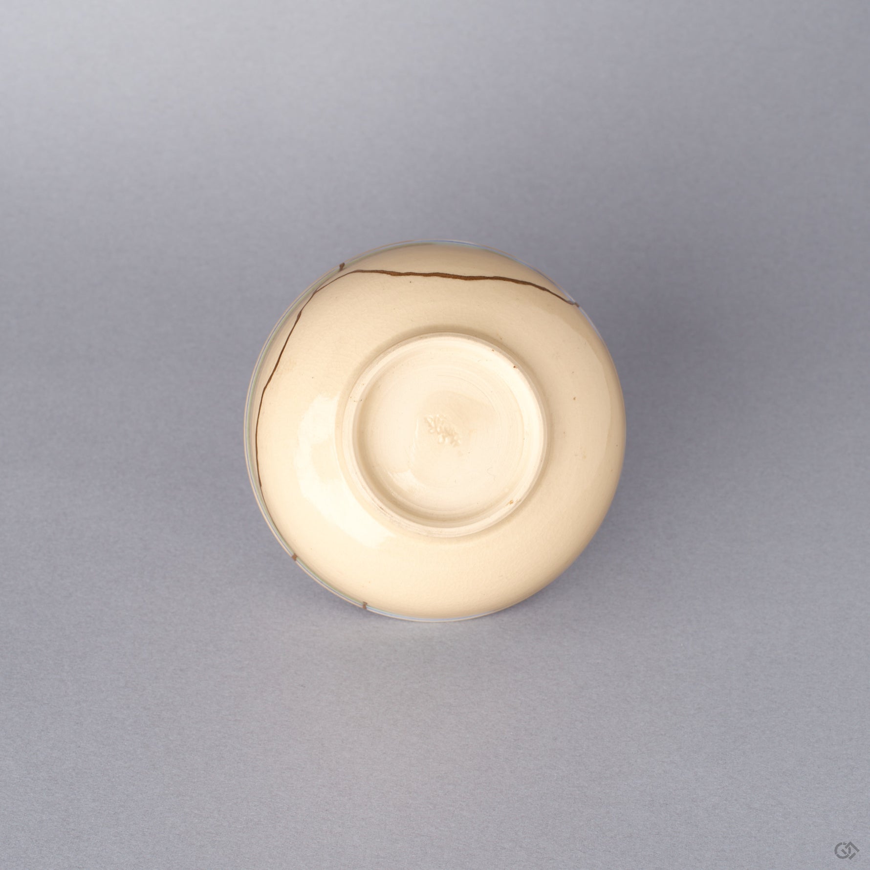 Bottom view of the cream colored Kyoto ware kintsugi cup, showing the small trimmed foot ring of the earthenware vessel restored with natural urushi and 24K gold.