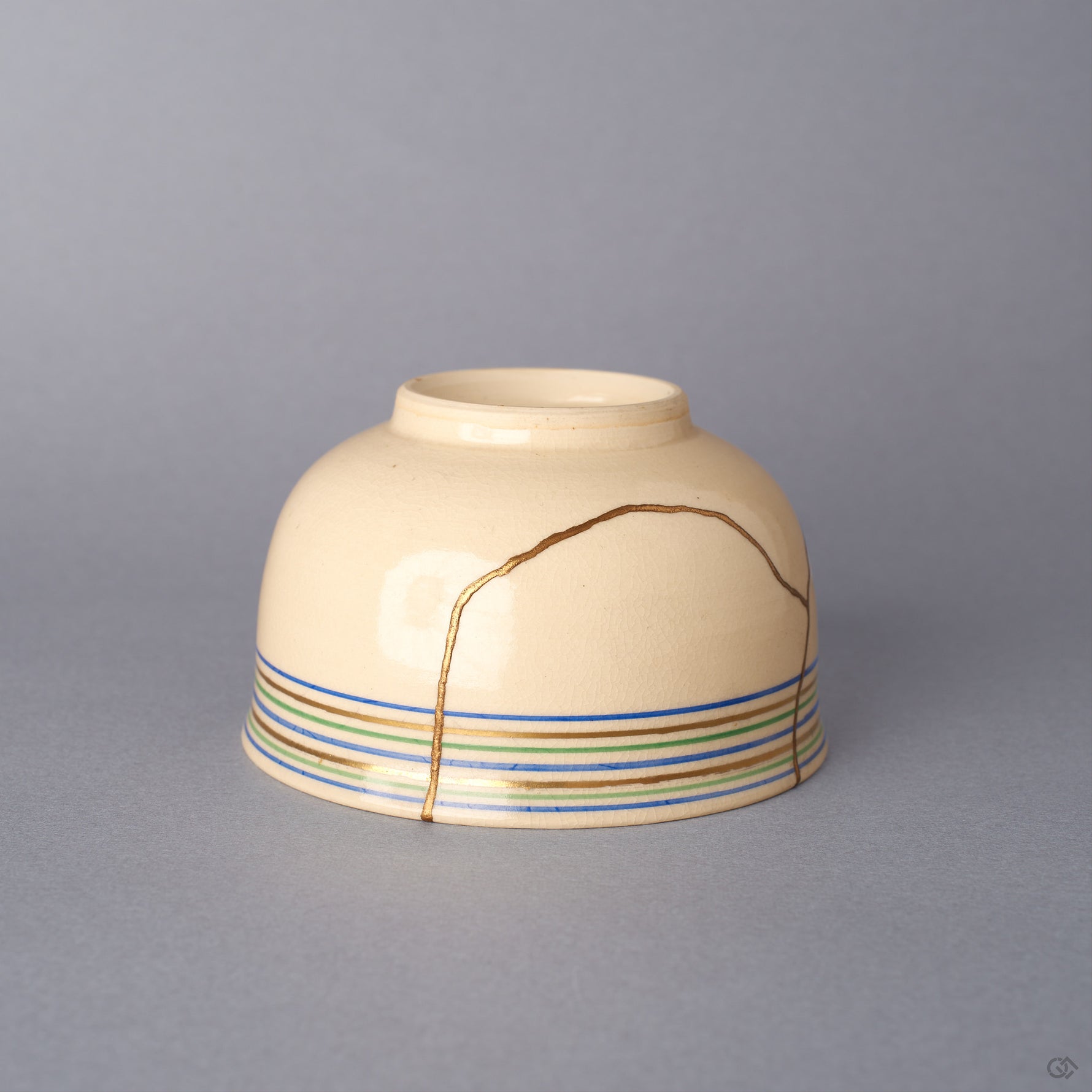 Side view of a cream colored Kyoto ware kintsugi cup, gold seams running from the rim down the body beneath fine koma-suji rim lines, restored in 24K gold and urushi.