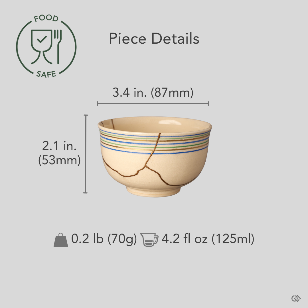 A cream colored Kyoto ware kintsugi cup held in hand for scale, showing its small cup size, koma-suji rim lines, and the seams restored in natural urushi and 24K gold.