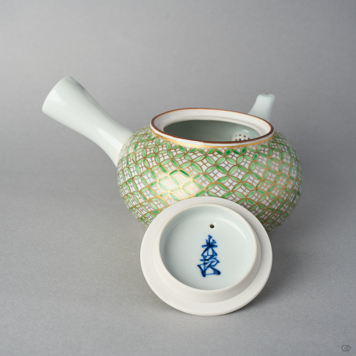 Underside of the Kyoto ware teapot lid, marked with a blue potter's signature, set before the open teapot body covered in a gold and green shippo pattern.